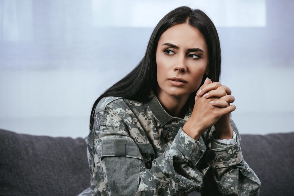 close-up portrait of thoughtful female soldier in military uniform with ptsd sitting on couch and